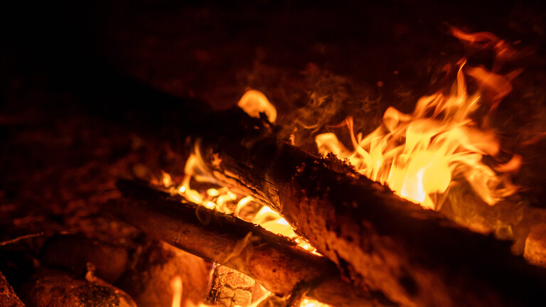 Nahaufnahme eines warm leuchtenden Lagerfeuers mit dicken, brennenden Ästen im Dunkeln