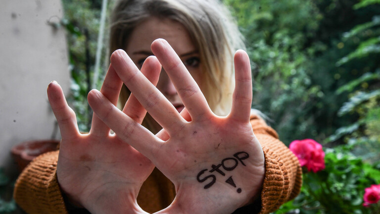 Frau hält Hände schützend vors Gesicht; auf einer Handfläche steht "Stop"