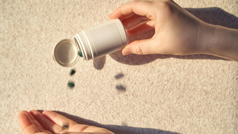 Weibliche Hände gießen grüne Pillen aus einer Dose in die Handfläche.