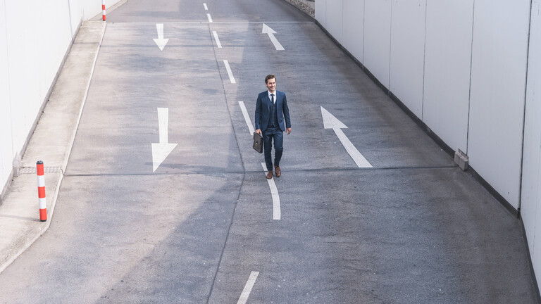 Ein Mann mit Anzug und Aktentasche läuft auf dem Mittelstreifen einer Straße