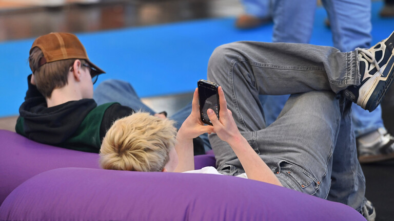 Zwei Jugendliche liegen auf Sitzsaecken und blicken auf ihre Smartphones