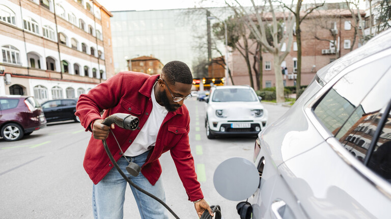Ein Mann ist dabei ein geparktes E-Auto an ein Stromladekabel zu hängen.