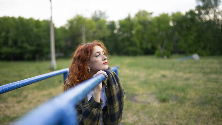 Rothaarige Frau lehnt sich im Freien an einen blauen Parallelbarren
