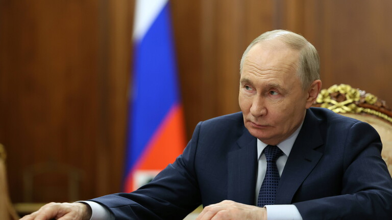 Russlands Präsident Putin sitzt an einem Tisch. Vor ihm liegt eine Mappe. Er blickt zur Seite. Im Hintergrund steht die russische Flagge.