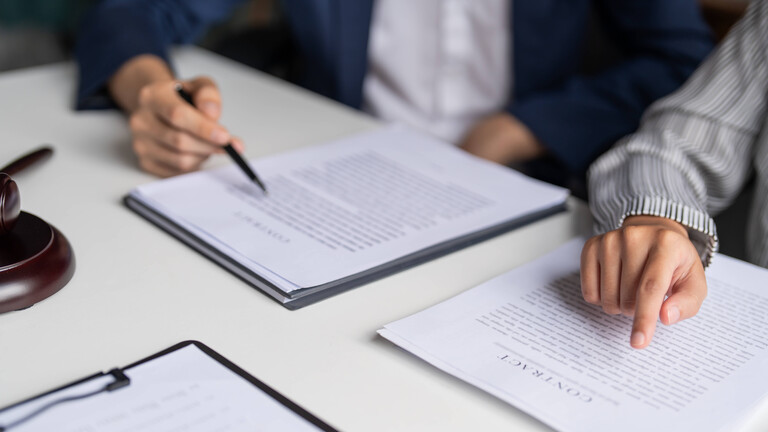 Junge Hände zeigen mit Stift auf Akten, vielleicht Verträge oder Gesetze.
