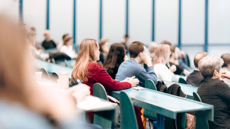 Rückansicht von Personen, die während einer Wirtschaftskonferenz oder eines Universitätsseminars in einem Hörsaal sitzen.
