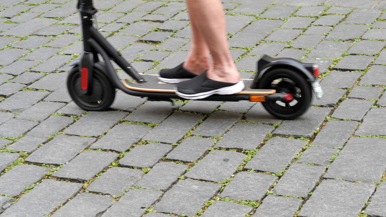 E-Scooter im Straßenverkehr, Jugendlicher fährt mit einem Elektroroller auf Straßenpflaster.