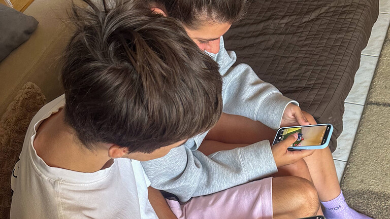 Junges Mädchen und Junge, die am 21. Juli 2026 auf ihren Smartphones in Paris soziale Medien nutzen.