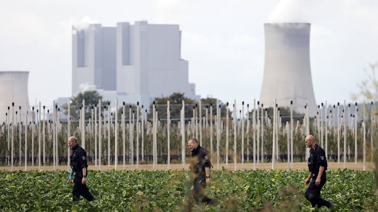 Nahe einem mutmaßlichen Anschlag auf ein Umspannwerk nahe Bergheim bei Köln durchsuchen Polizisten umliegende Felder. Im Hintergrund ist ein Kraftwerk zu sehen.
