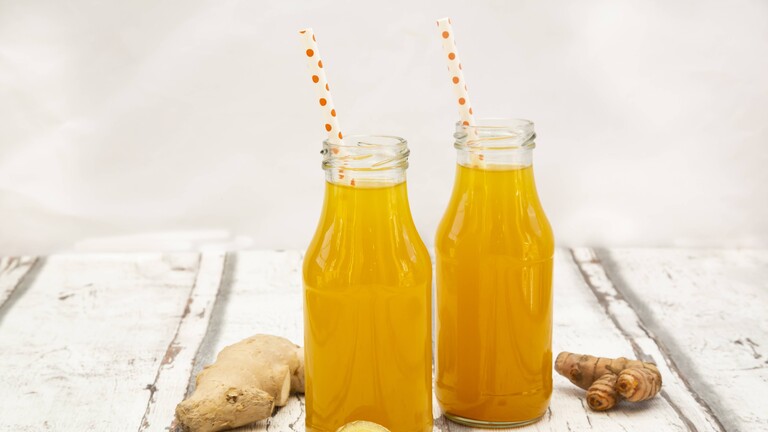 Ingwershot mit Orange und Kurkuma auf weißem Holztisch