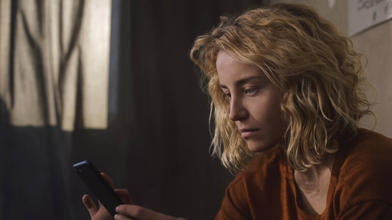 Foto einer jungen Frau, die ernst auf ihr Smartphone blickt