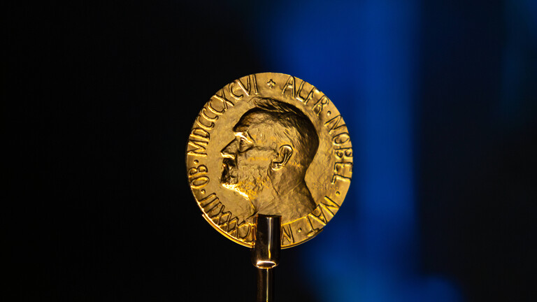 Eine goldene Medaille vor schwarzem Hintergrund. Darauf ist ein Männerkopf im Profil.