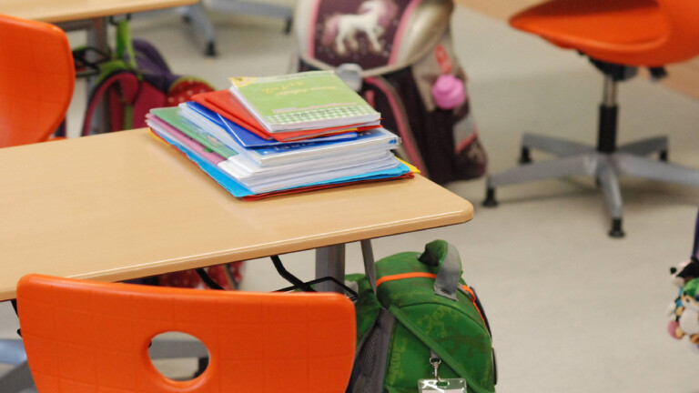 Ein Klassenzimmer in einer Schule in Leipzig. Auf einem Tisch liegen Hefte, davor steht ein orangefarbener Stuhl