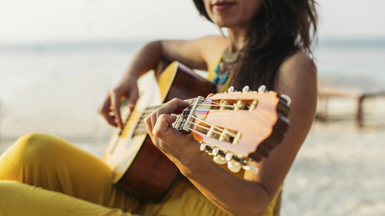 Frau spielt Gitare am Strand