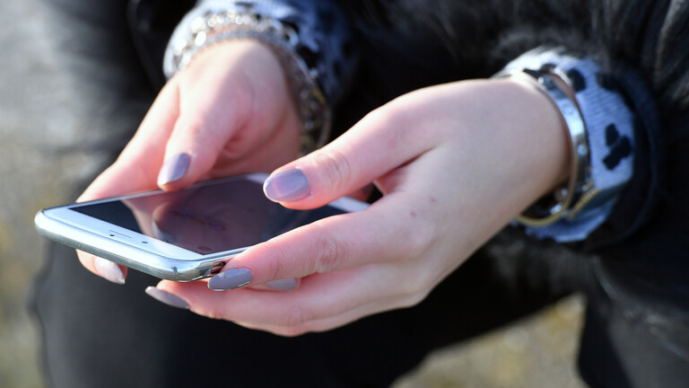 Person hält Smartphone in Händen, deren Fingernägel lang sind und lila lackiert sind