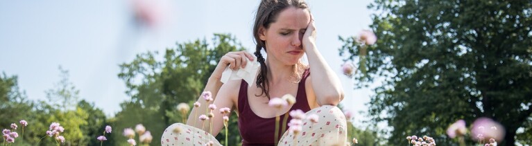 Frau sitzt im Feld mit Heuschnupfen