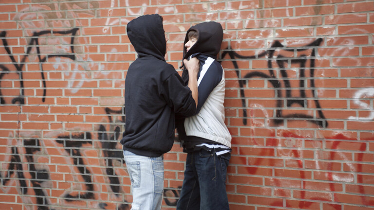 Ein Teenager drückt einen kleineren gewaltsam gegen eine Wand, gestellte Szene