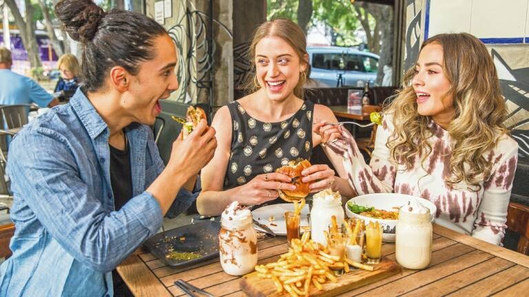 Personen zelebrieren ihre Freundschaft im Restaurant. Sie essen auf der Terrasse Snacks und lachen beim Essen.