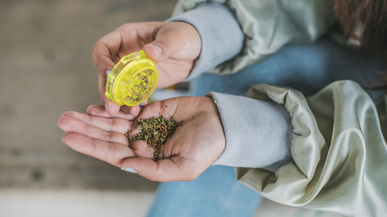 Eine Frau kippt aus einer gelben Dose eine Portion Cannabis auf ihre Handfläche.