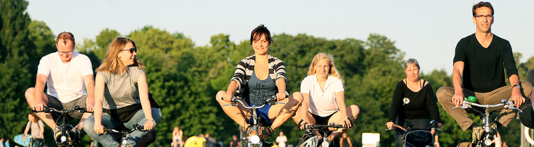 Lachende Menschen machen Yoga-Übungen auf dem Fahrrad