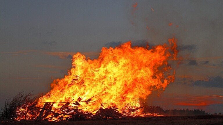 Ein Feuer brennt in einer Landschaft. Am Horizont sind Bäume zu sehen.