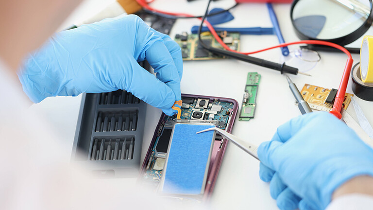 Hände mit Schutzhandschuhen tauschen den Akku an einem Smartphone aus.