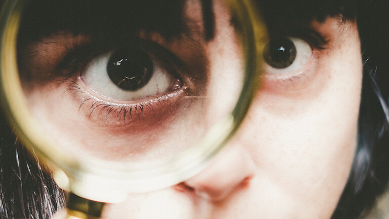 Junge Frau guckt durch ein Vergößerungsglas.