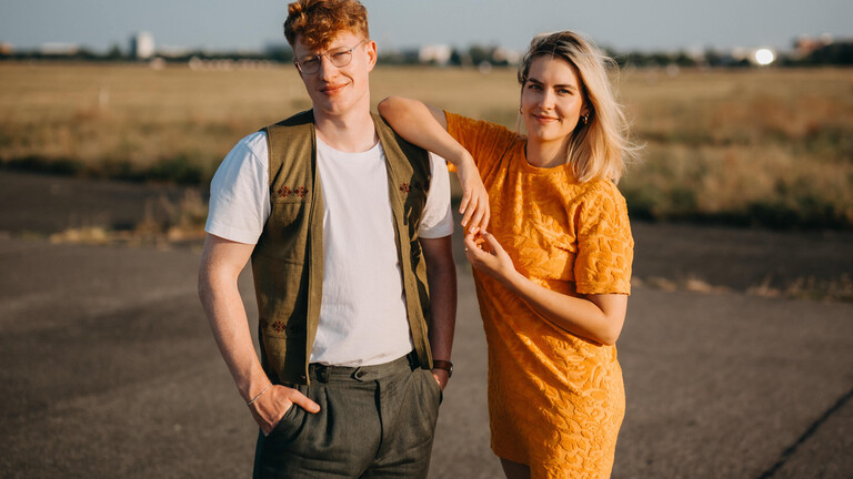 Die beiden Hosts vom Deutschlandfunk-Nova-Podcast "Facts und Feelings" stehen nebeneinander auf dem Tempelhofer Feld in Berlin. Die Hosts sind Przemek Żuk und Shalin Rogall.