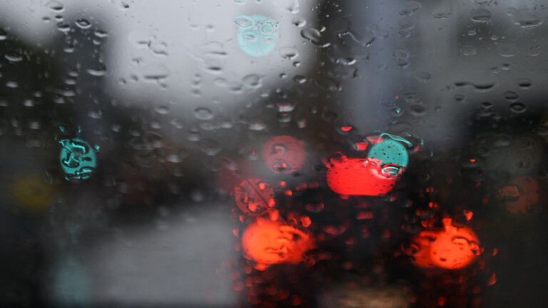 Rücklichter eines Autos und grüne Ampeln sind durch die verregnete Windschutzscheibe eines Autos zu sehen