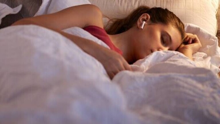Eine Frau schläft im Bett auf der Seite und trägt weiße In-Ear-Kopfhörer.