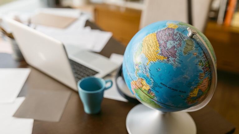Globus neben Laptop, Kaffeetasse und Kartons