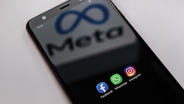 Auf einem Smartphone sind die Apps von Facebook, Whatsapp und Instagram zu sehen. Auf dem Bildschirm spiegelt sich der Schriftzug plus Logo von Meta.
