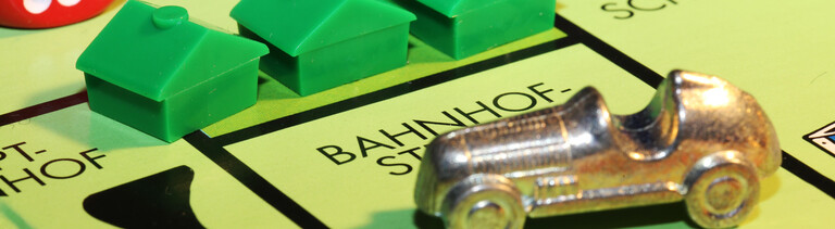 Ein Monopoly-Auto und drei Häuschen auf einem Spielfeld