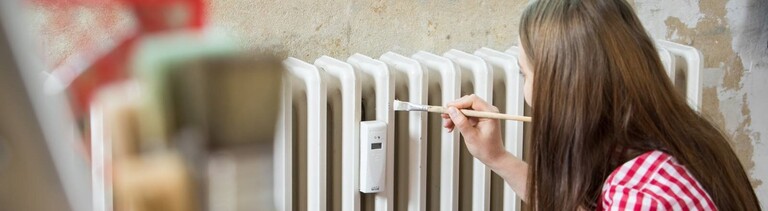 Eine junge Frau streicht in einer Wohnung eine Heizung mit weißer Farbe