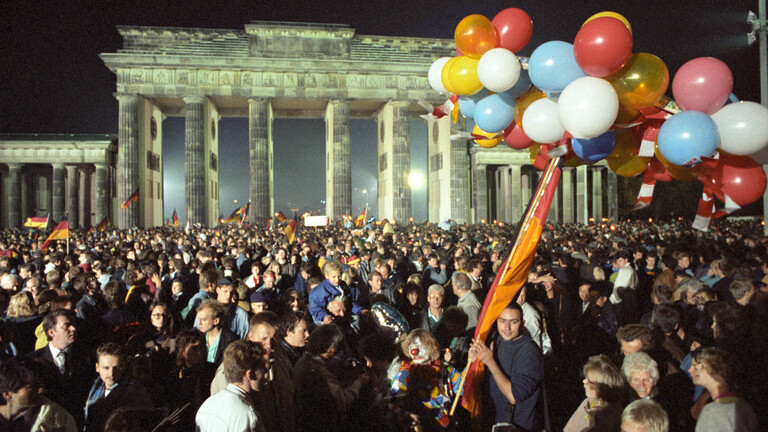 Eine Menschenmange feiert mit Luftballons und Deutschlandfahnen vor dem Brandenburger Tor die Wiedervereinigung in der Nacht auf den 3. Oktober 1990
