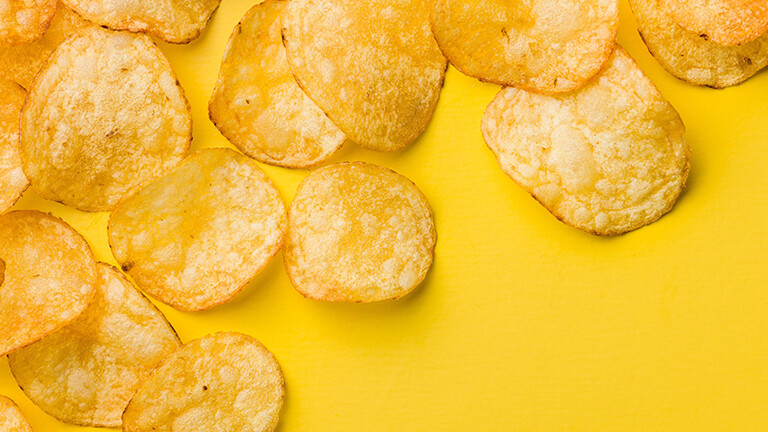 Eine Handvoll Kartoffelchips liegen auf einem gelben Tisch.