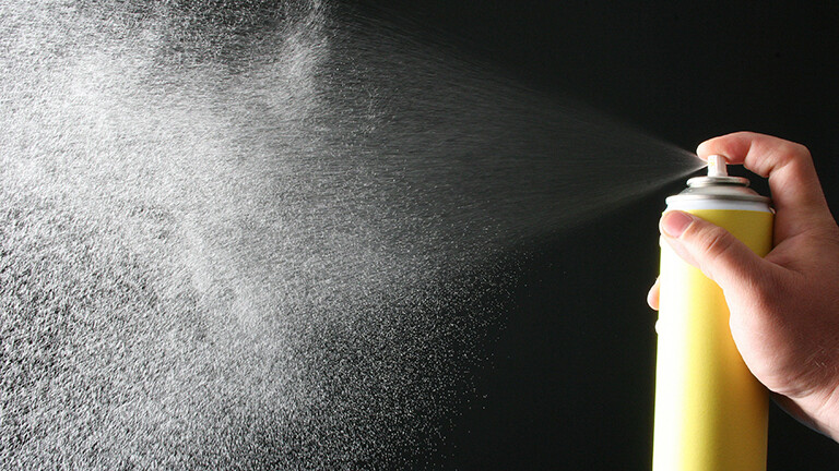 Eine Hand hält eine gelbfarbene Spraydose und sprayt. Der Sprühnebel ist gut erkennbar.