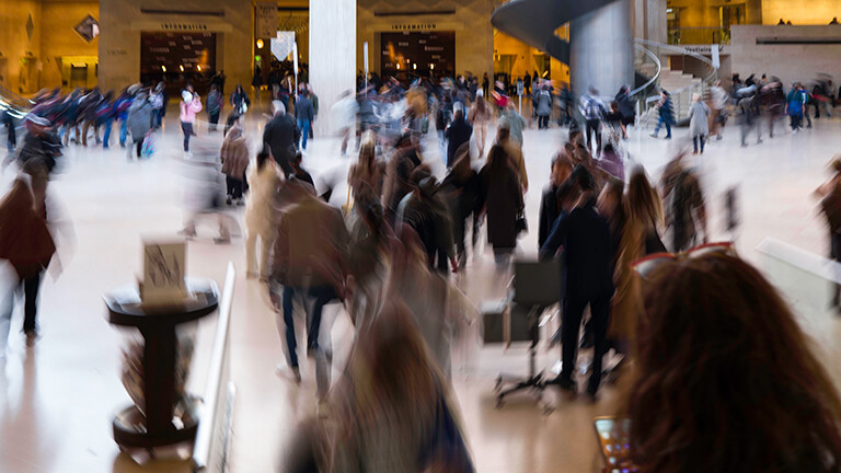 Viele Menschen stehen in einem hohen Raum, eine Wendeltreppe führt nach oben. Ihre Bewegungen sind unscharf. Es ist die Glaspyramide, Haupteingang zum Museum Louvre.