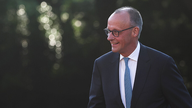 Bundeskanzler Friedrich Merz läuft im Freien, er lächelt. Er trägt einen Anzug. Aufnahme am Rande des Nato-Gipfels am 24. Juni 2025.