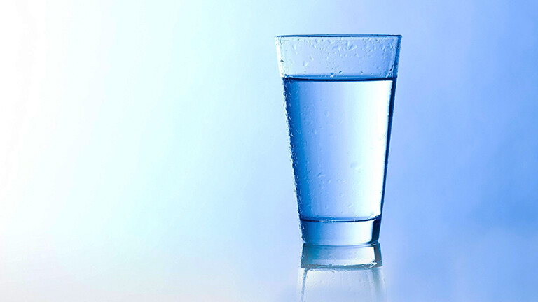 Ein gefülltes Wasserglas vor blauem Hintergrund.