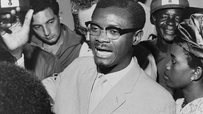 Schwarz-weiß-Foto: Im Oktober 1960 steht Kongos Premierminister Patrice Lumumba in einer Menschentraube und spricht zu seinen Anhängern. Er trägt eine Brille und Anzug.