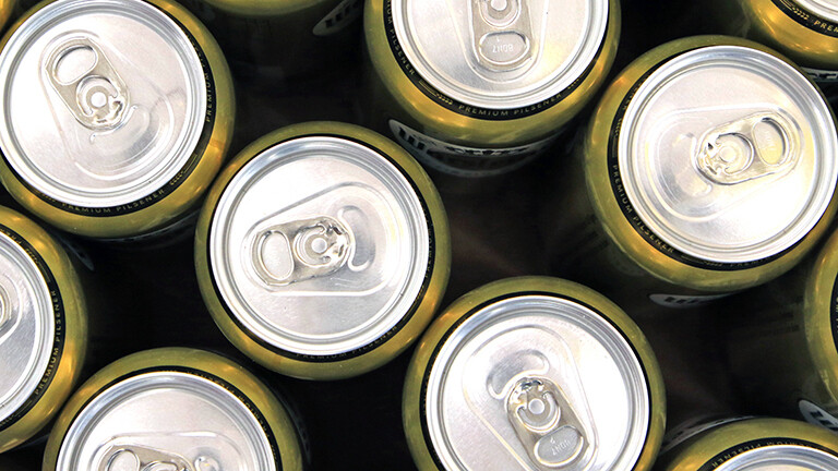 Mehrere noch geschlossene Bierdosen stehen nebeneinander; sie sind goldfarben. Der Blick fällt von oben auf die Dosen.