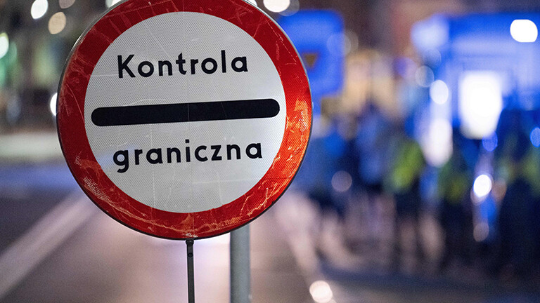 Auf einem runden Schild steht "Kontrola graniczna", polnisch für Grenzkontrolle. Im Hintergrund sind unscharf polnische Grenzschützer zu sehen.