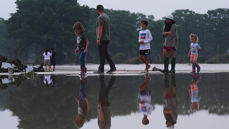 Nach den Überschwemmungen im US-Bundesstaat Texas läuft eine Familie durch Wasser, sie spiegeln sich im Wasser.