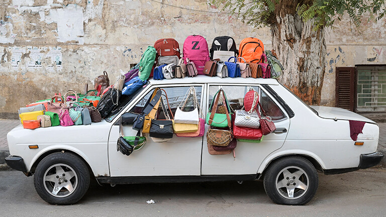 Auf einem alten weißen Auto stehen auf Dach und Autohaube viele bunte Taschen, auch an den Fenstern hängen Taschen. Es sind Fake-Taschen, die zum Verkauf angeboten werden, in der ägyptischen Stadt Assiut.