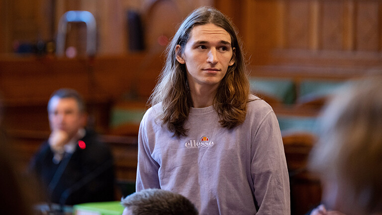 Maja T. steht im Gerichtssaal des Stadtgericht in Budapest. Die Wände sind holzvertafelt. Maja T. steht, Maja T. hat braune, lange Haare und trägt einen fliederfarbenen Pullover.