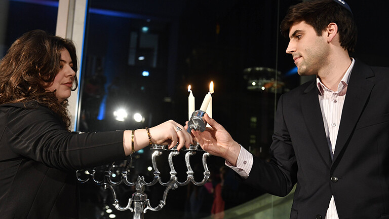 Zur ersten Chanukka-Feier im Deutschen Bundestag steht Ron Dekel im Veranstaltungsfoyer des Marie-Elisabeth-Lüders-Hauses; er zündet zusammen mit Naomi Tamir eine Kerze an; es ist die zweite Kerze eines Chanukka-Leuchters.