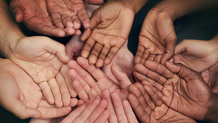 Viele Hände mit verschiedenen Hautfarben liegen übereinander, es wirkt nach Gemeinschaft.