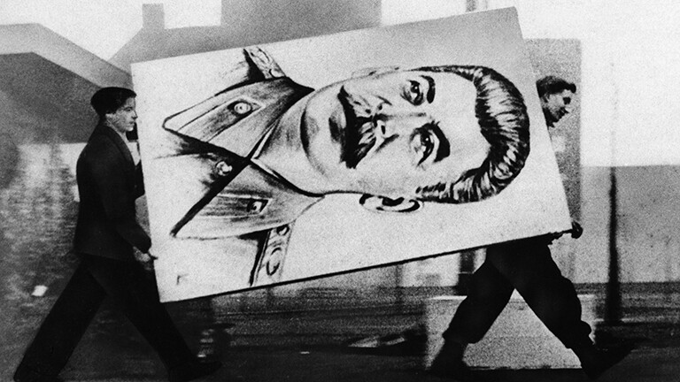 Archivfoto in schwarz-weiß aus dem Jahr 1956: Zwei Männer tragen ein Plakat mit dem Konterfei des Diktators Stalin weg.