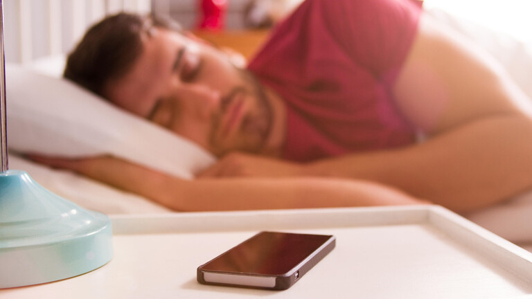 Ein Mann schläft im Bett, vor ihm ein Smartphone